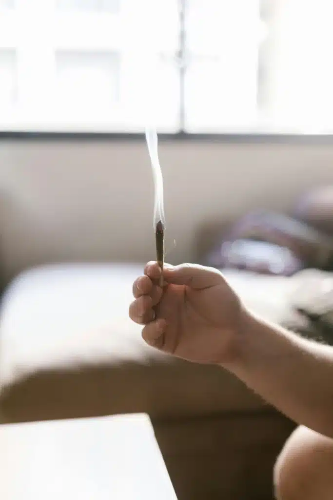 Main tenant un petit joint fumant de résine CBD sans THC, avec un arrière-plan flou d'une fenêtre et un intérieur.