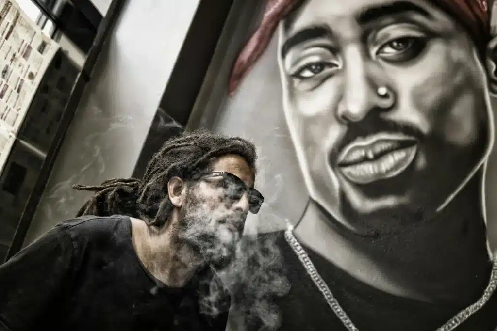 Homme aux dreadlocks fumant de la résine CBD devant une fresque murale – BUDDY BOO
