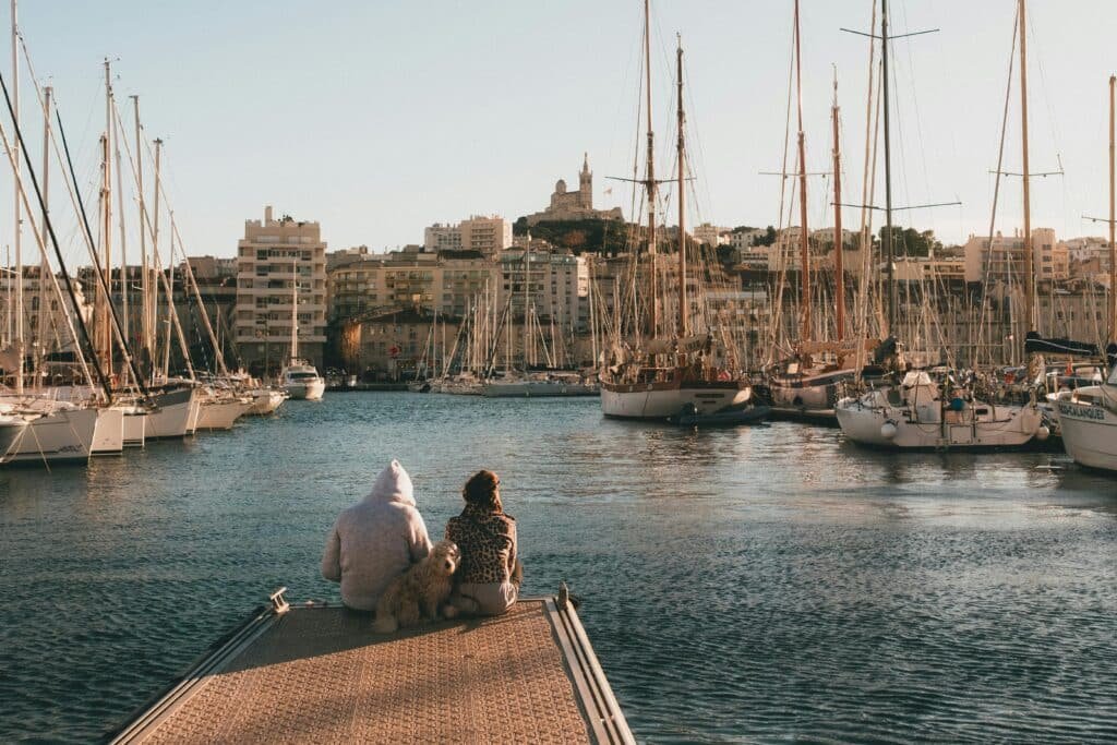 Vue du Vieux-Port de Marseille avec deux personnes et un chien face aux bateaux, illustrant la détente et le bien-être offerts par les fleurs CBD BUDDY BOO