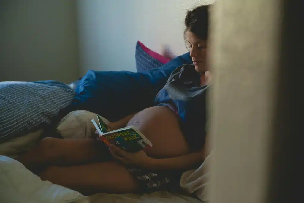 Femme enceinte lisant paisiblement dans son lit, évoquant la sérénité et la réflexion autour du CBD grossesse selon BUDDY BOO.