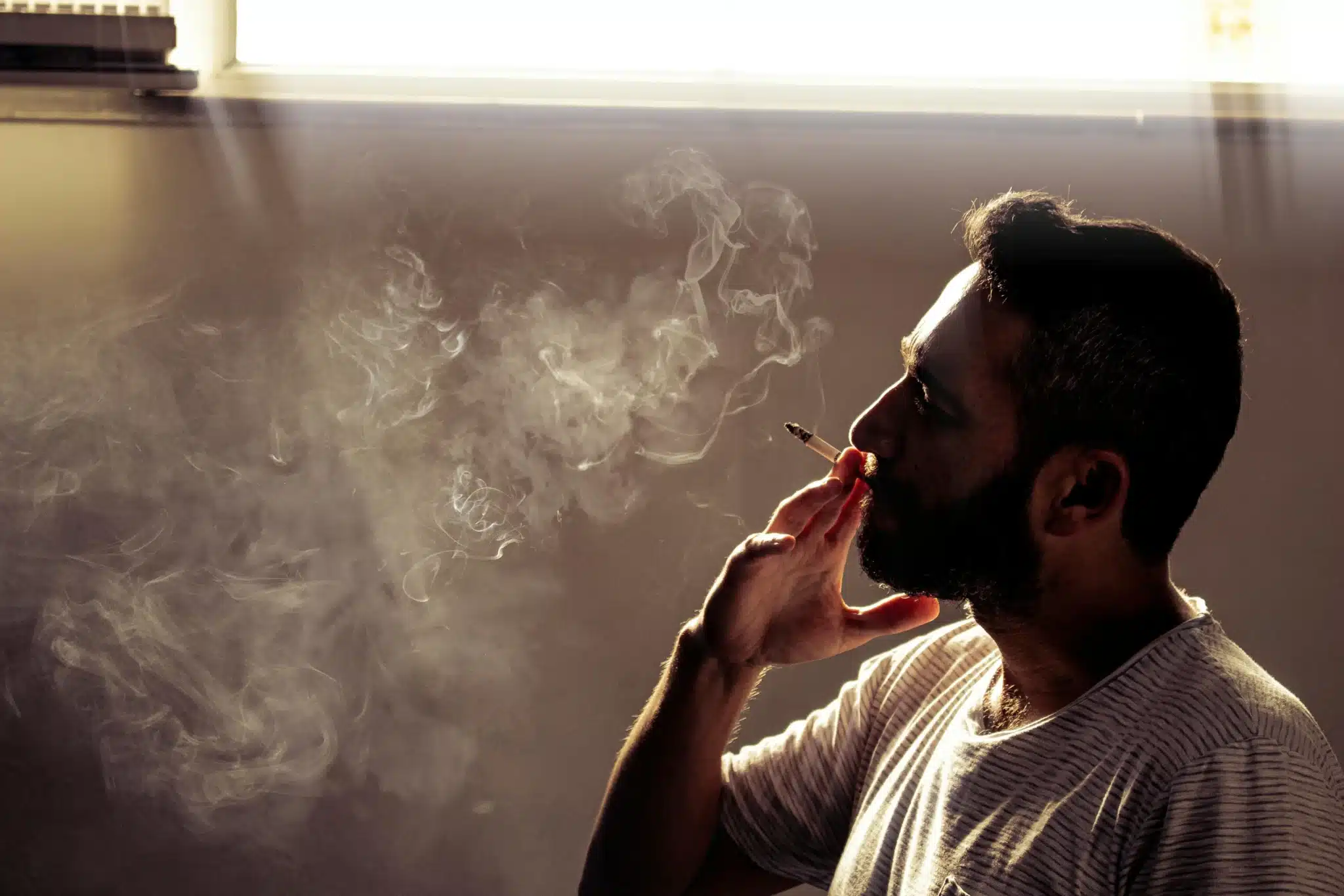 Homme fumant un joint dans une lumière dorée, illustrant la détente et la qualité du hash CBD sans THC proposé par BUDDY BOO.