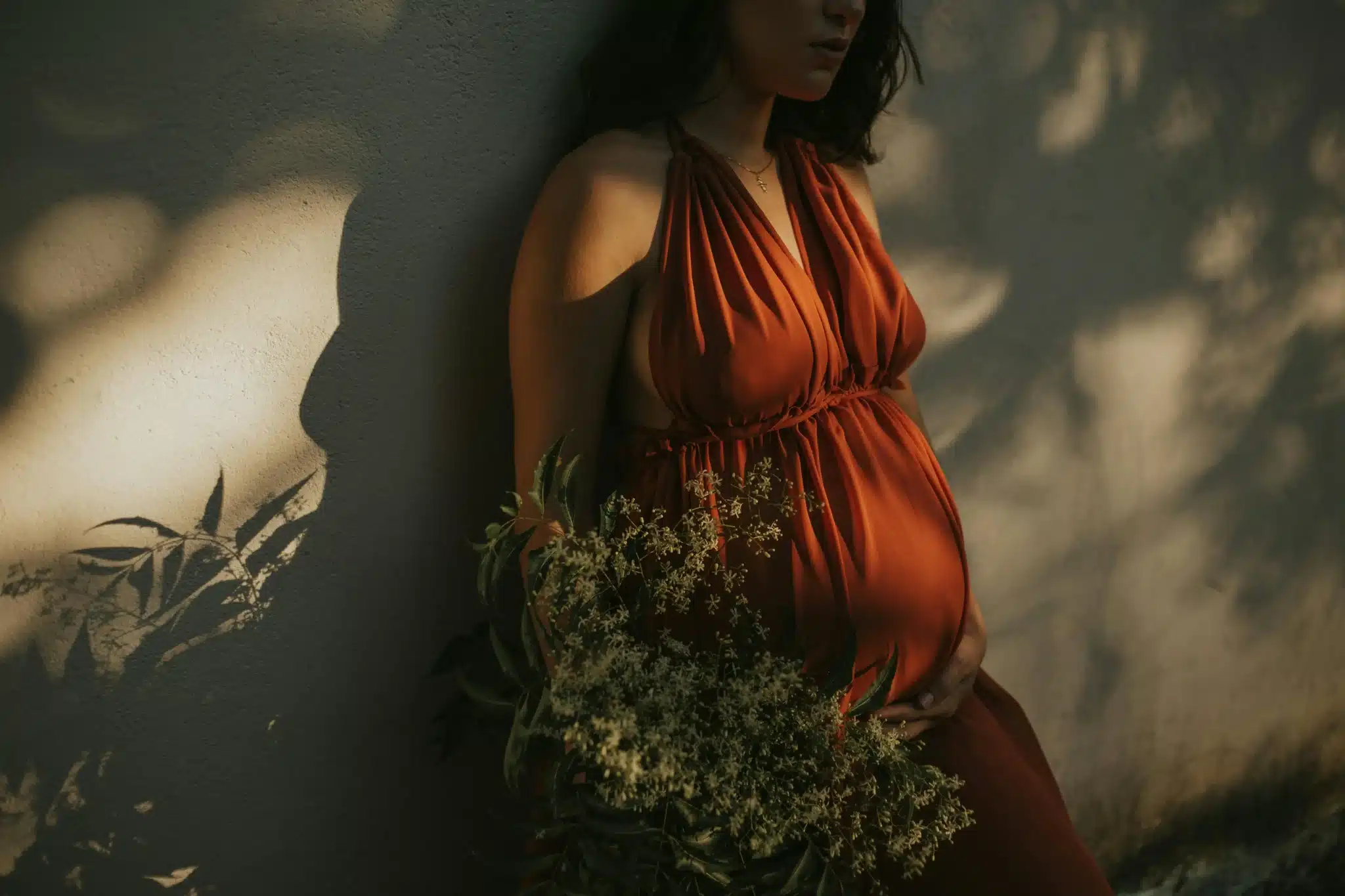 Femme enceinte en robe orange tenant des fleurs, incarnant la naturalité et la douceur du CBD grossesse selon BUDDY BOO.