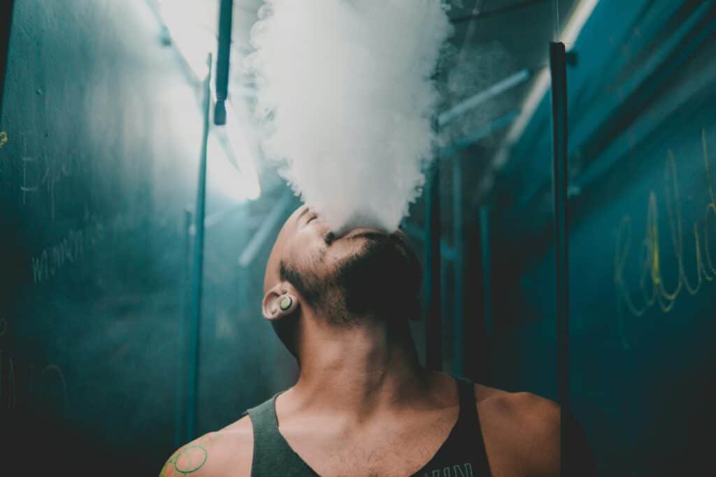 Personne utilisant un vaporisateur CBD BUDDY BOO, exhalant une vapeur dense dans une ambiance urbaine