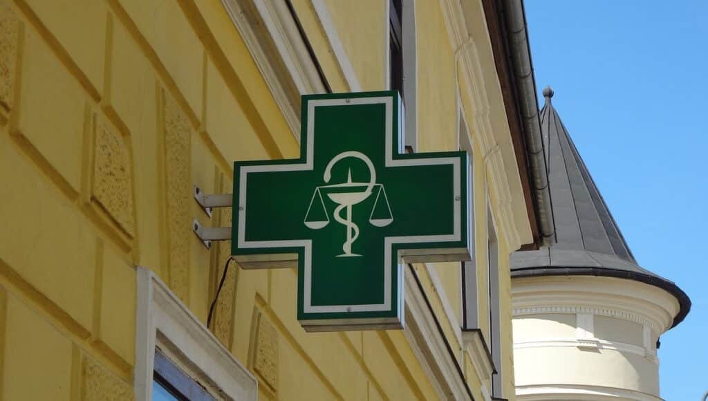 Croix verte de pharmacie accrochée sur un bâtiment, utilisée pour illustrer le sujet CBD pharmacie avec la marque BUDDY BOO.